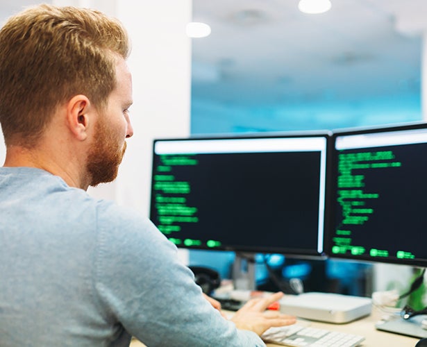 A man works at a computer with two monitors.